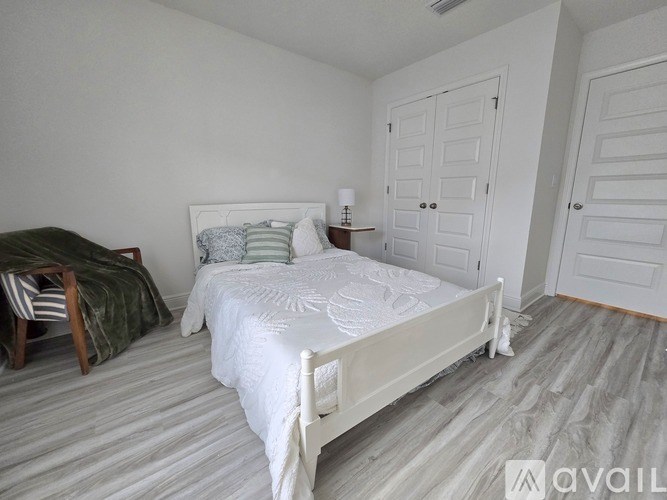 A bedroom with a white bed and a chair with a green blanket.