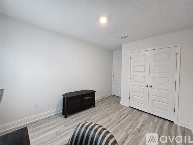 A room with a wooden floor and a white wall with a black bench and a white door.