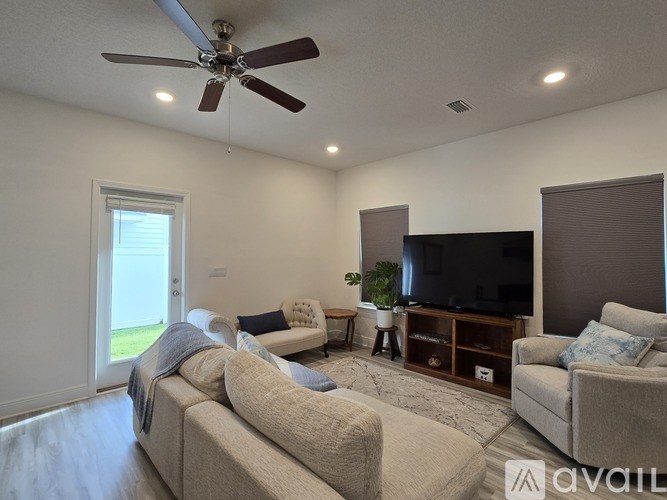 A living room with a beige couch, a television, and a ceiling fan.