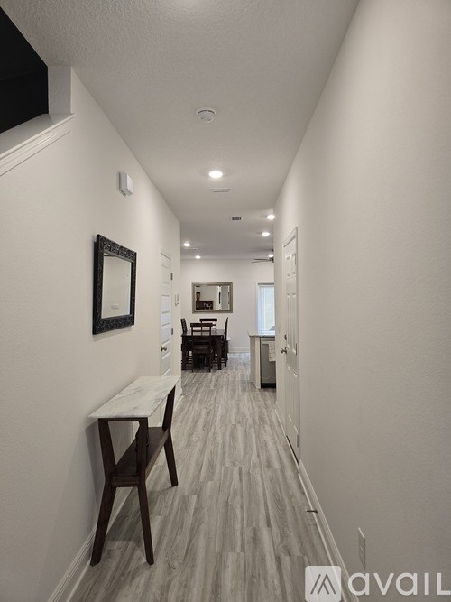 A long hallway with a table and chairs on the left and a mirror on the wall.