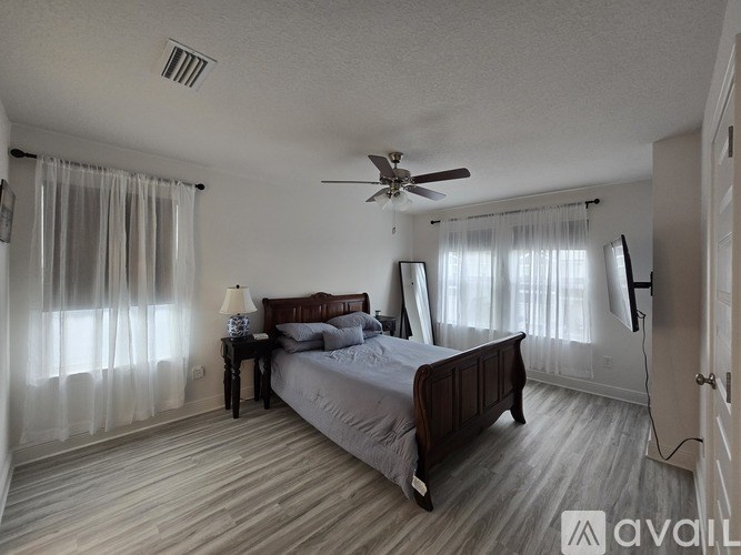 A bedroom with a bed, a table with a lamp, and a ceiling fan.