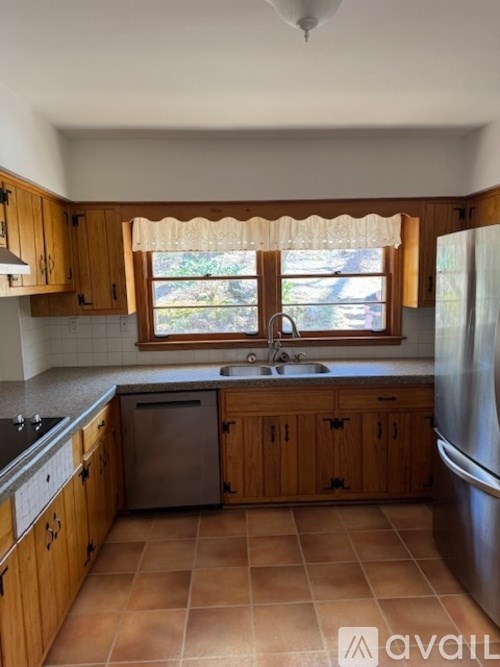 A kitchen with wooden cabinets and a window with a lace curtain.