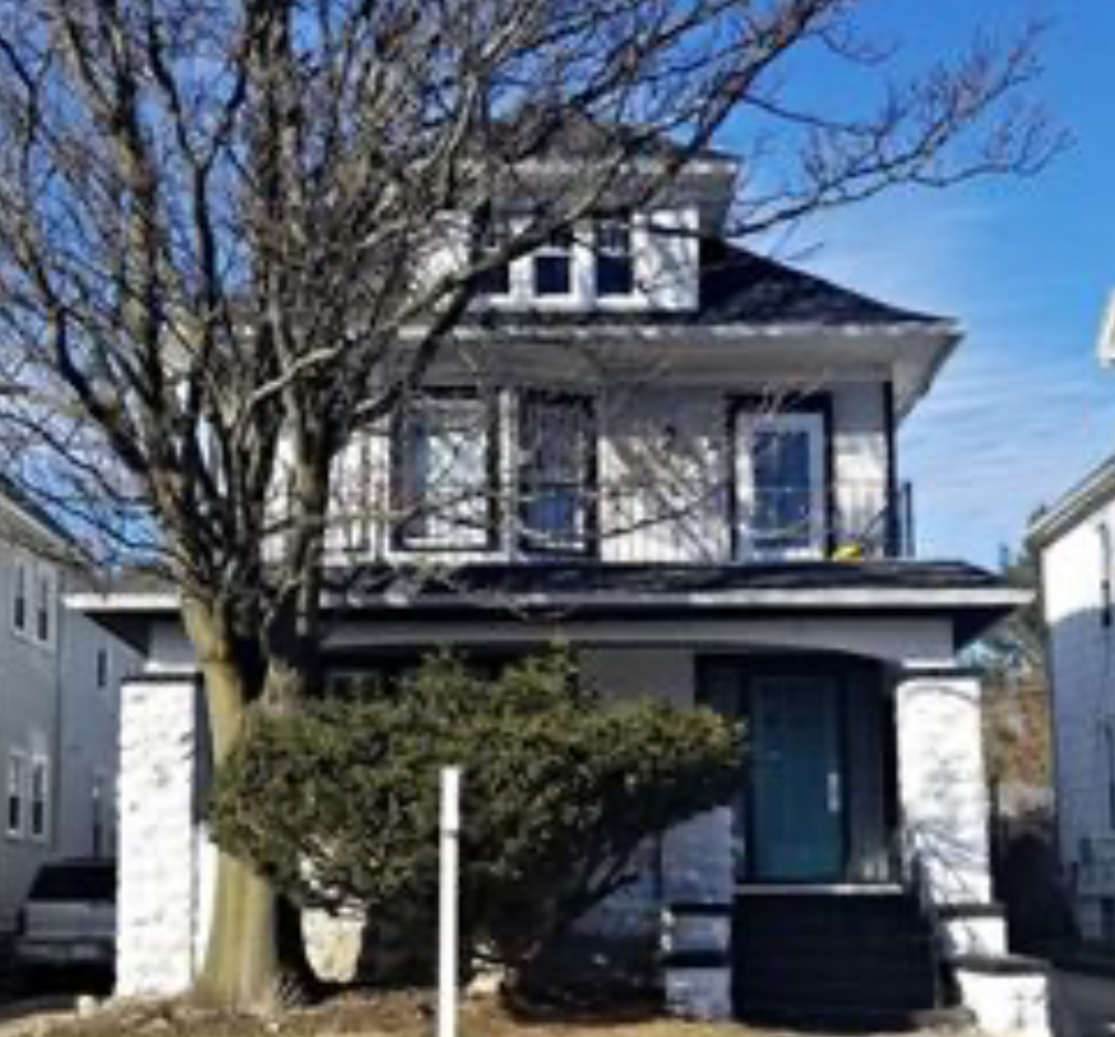 A white house with a black roof and a balcony.