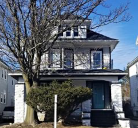 A white house with a black roof and a balcony.