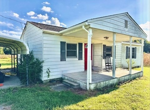 A small white house with a red door and a porch.