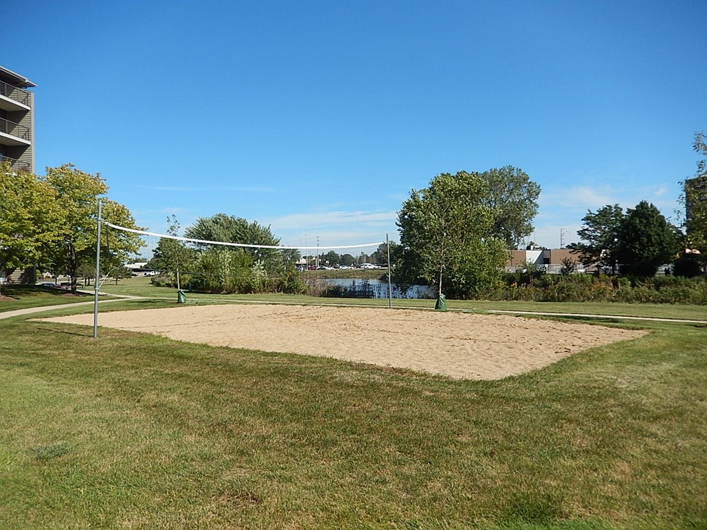 A sand volleyball court is surrounded by trees and apartment buildings.