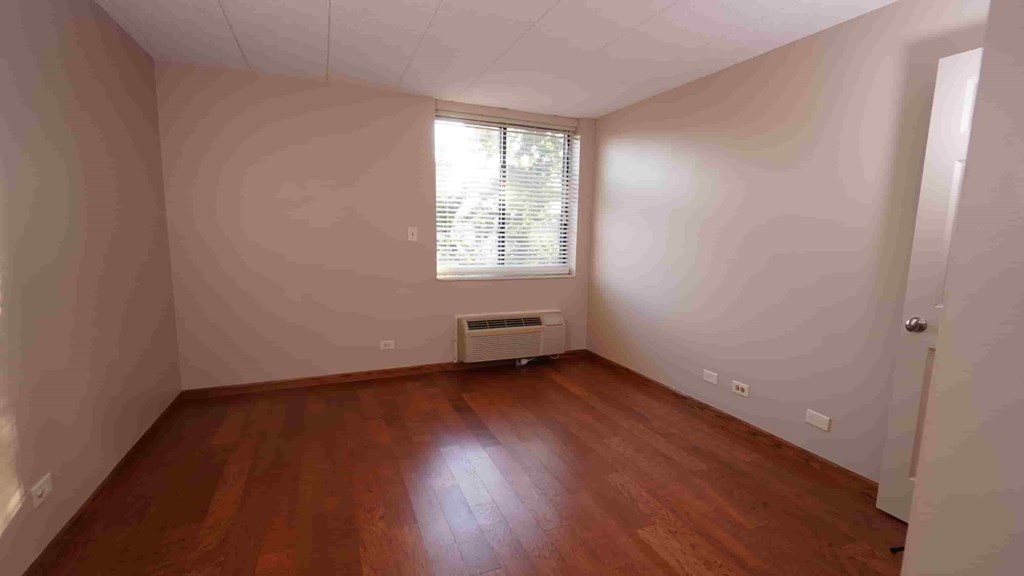 A room with wooden floors and a window with blinds.
