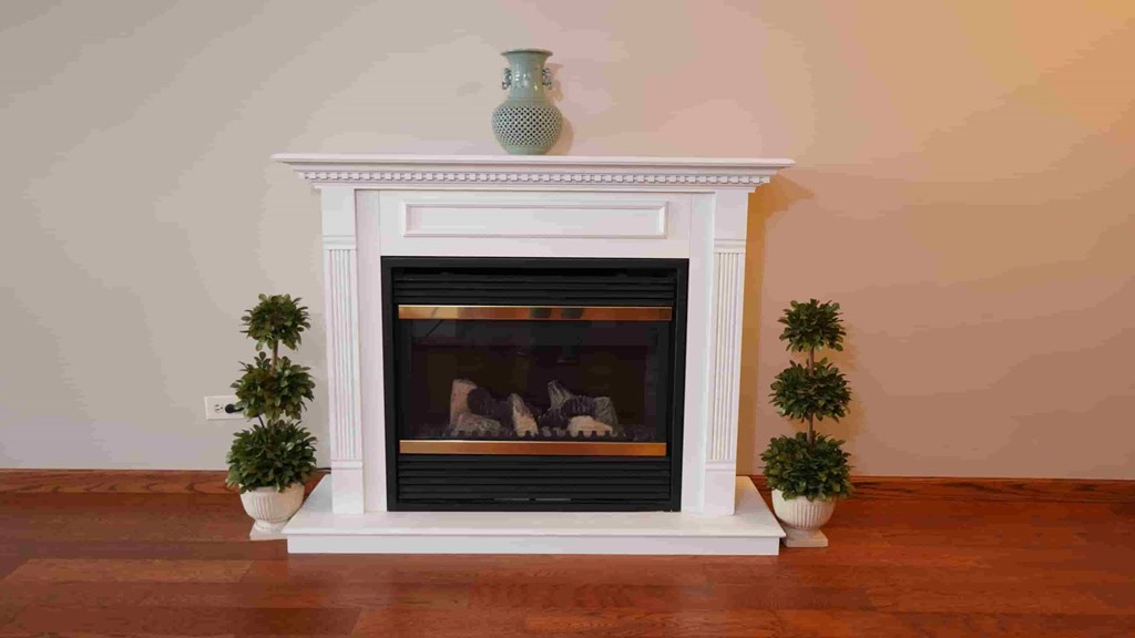 A white fireplace with a vase on top and two small trees on either side.