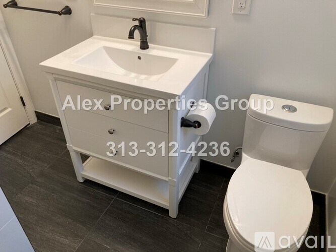 A white sink and toilet in a bathroom with a Alex Properties Group sign and phone number.