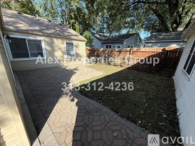 A backyard with a brick patio and a house with a sign that says Alex Properties Group.