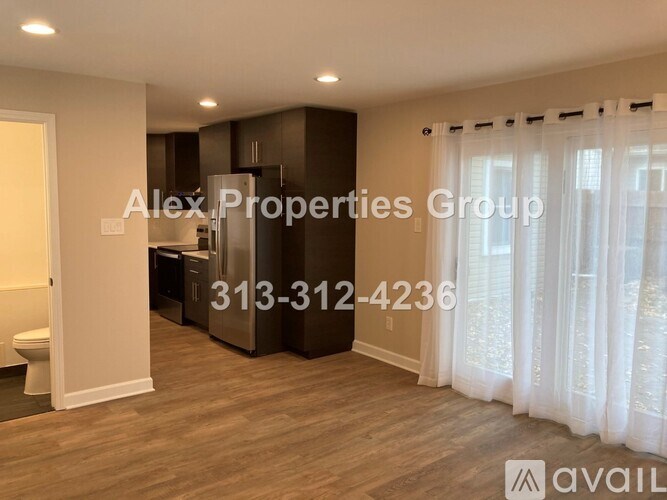 A room with a toilet, a kitchen, and a window with curtains.