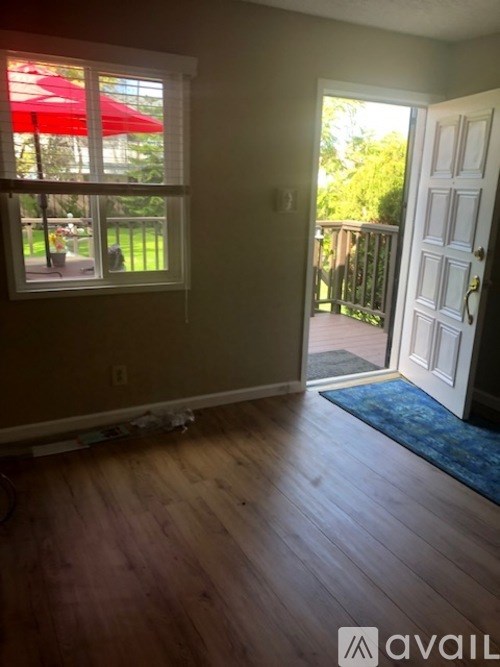 A room with a wooden floor and a red umbrella outside the window.