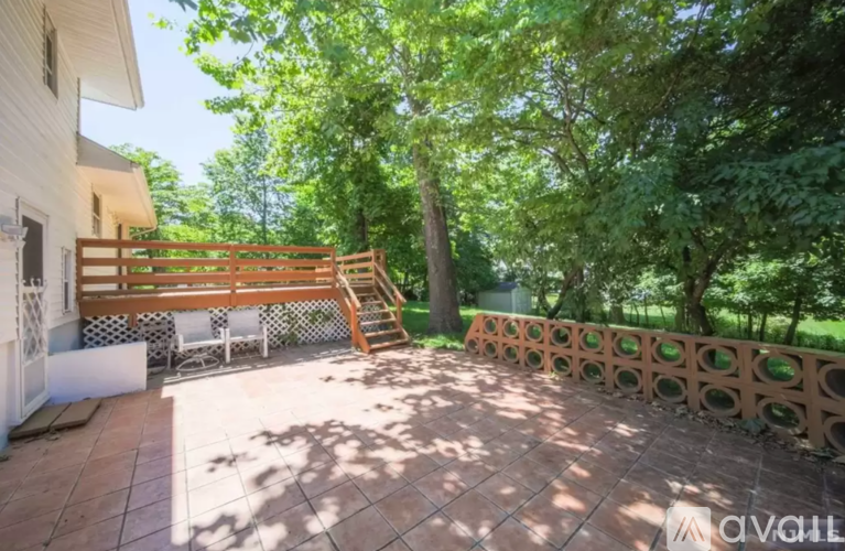 A patio with a wooden railing and a white chair is surrounded by trees.