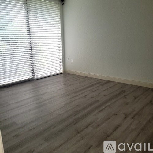 A room with wooden flooring and white blinds on the window.