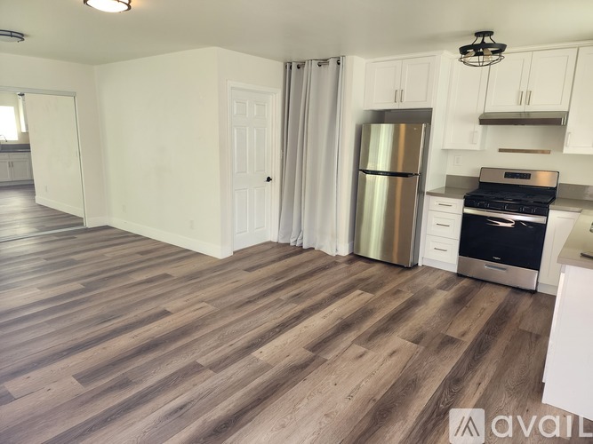 A room with wooden flooring and a white wall with a door.
