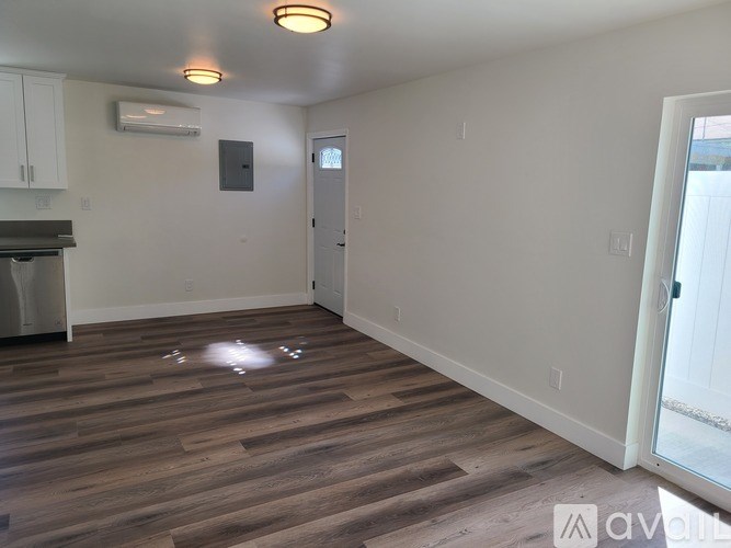 A room with wooden flooring and a white wall with a door.