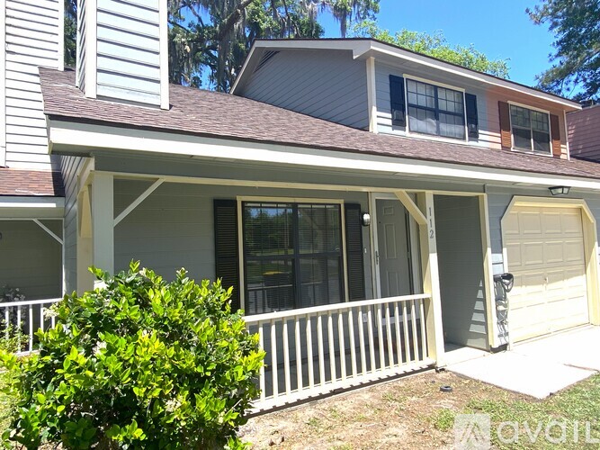 A house with a white porch and a green bush in front.