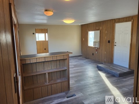 A room with wooden walls and a wooden floor with a shelf and a door.