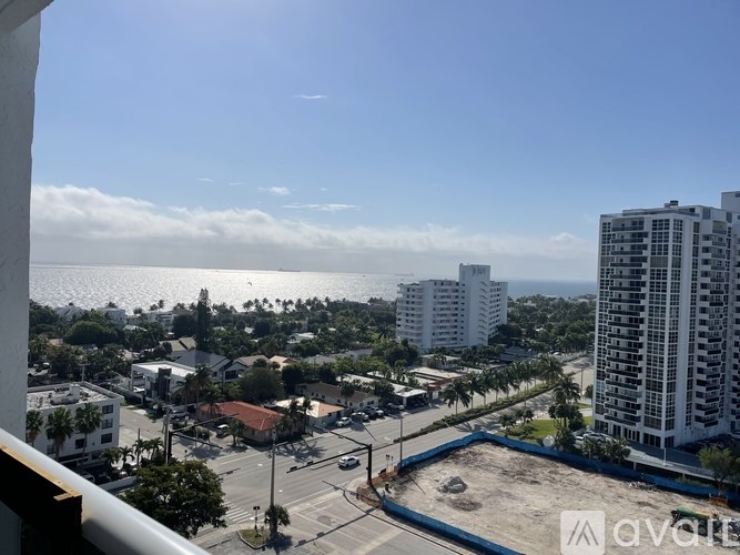 A view from a balcony overlooking a city street with buildings and a clear sky.