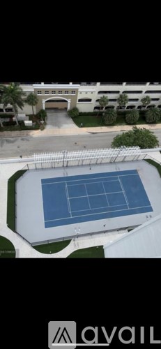 A tennis court is located in the middle of a parking lot.