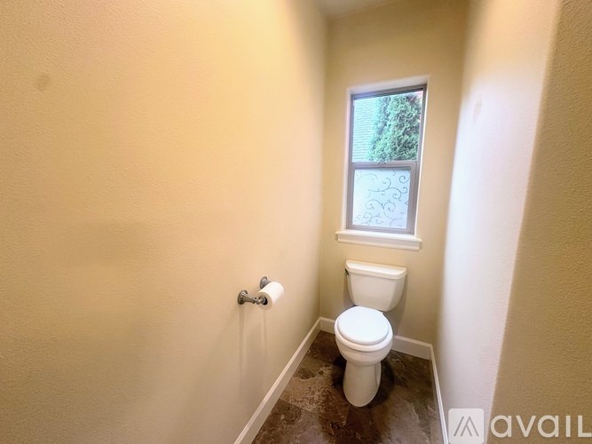 A room with a carpeted floor and a large window with a view of a street and houses.
