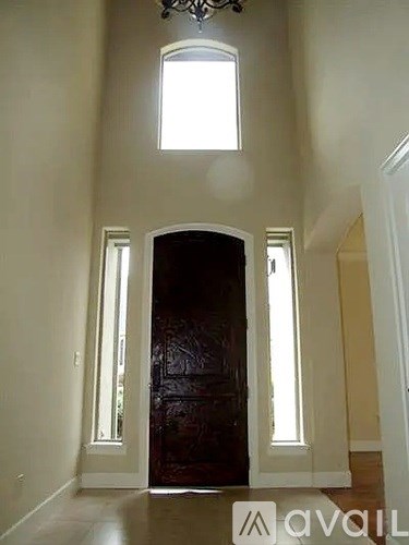 A chandelier hangs from the ceiling in a room with a brown door and two windows.