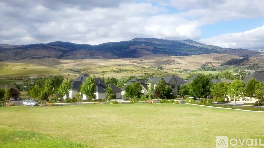 A grassy field with houses and mountains in the background.