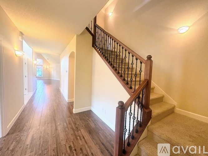 A hallway with a staircase and light wood flooring.