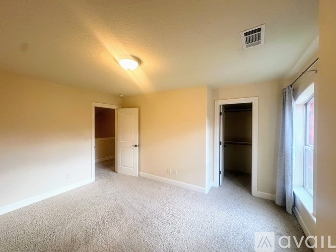 A carpeted room with a window and two doors.
