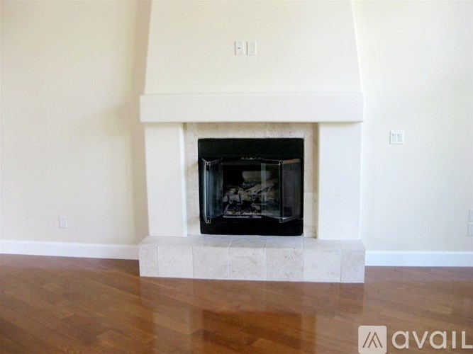 A fireplace with a white mantle and a black firebox is in the middle of a room with wooden flooring.
