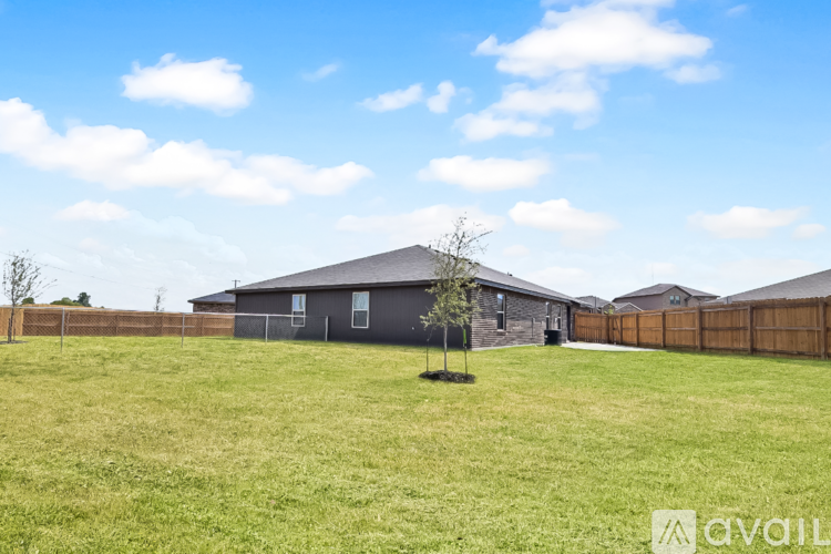 A grassy field with a wooden fence and two buildings in the background.