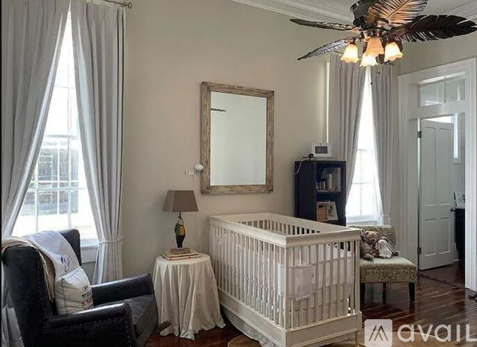 A baby nursery with a crib, chair, and a ceiling fan.