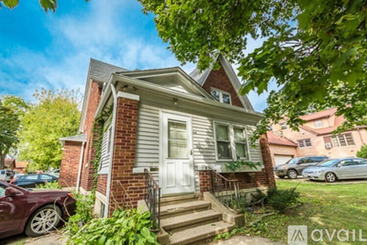 A house with a white door and a brick chimney is surrounded by greenery.