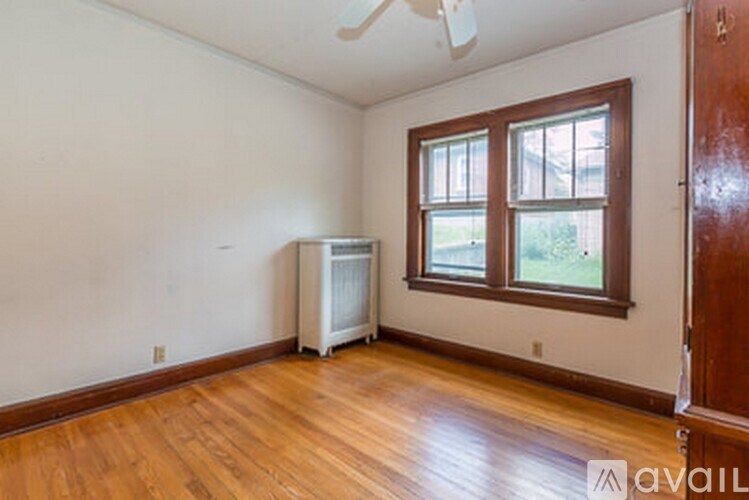 A room with a wooden floor and a window with a white fan on the ceiling.