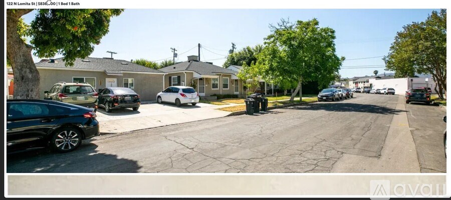 A street view with cars parked on the side of the road and houses in the background.