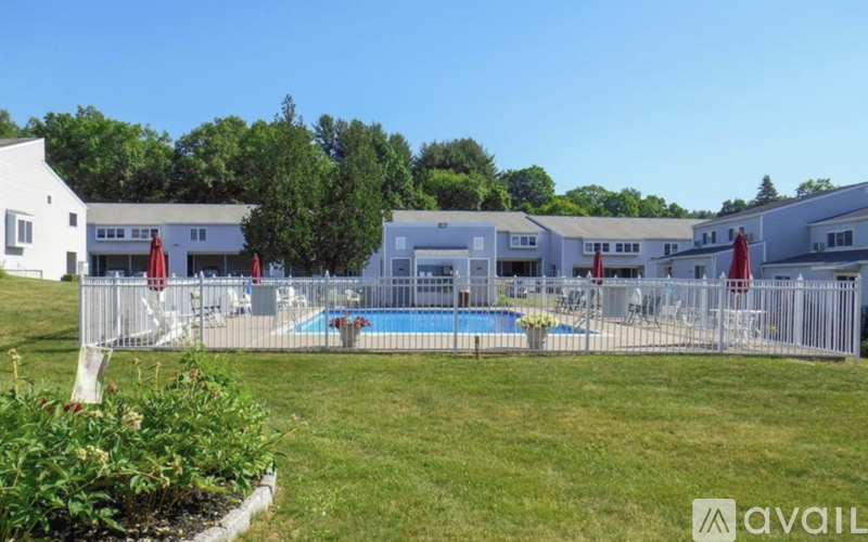 A pool surrounded by a fence and chairs with a building in the background.
