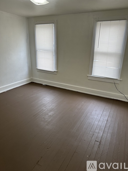 A room with wooden flooring and two windows.