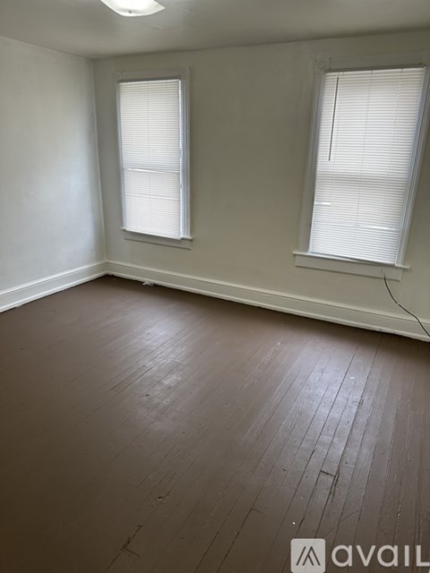 A room with wooden flooring and two windows.