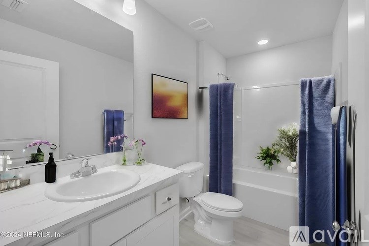A white bathroom with a white toilet, a white sink, a white vanity, a white bathtub, a white towel, a white shower curtain, a white bathtub faucet, a white to
