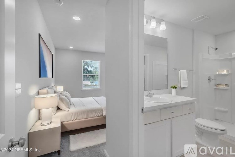 A white bedroom with a bed, nightstand, and a mirrored vanity.