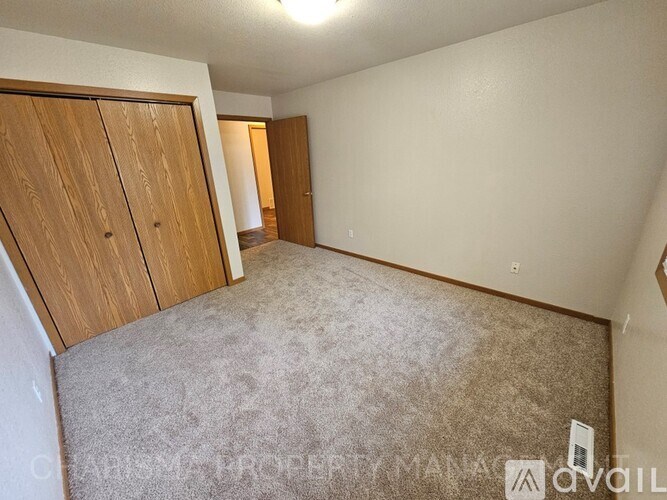 A bedroom with a carpeted floor and a wooden wardrobe.