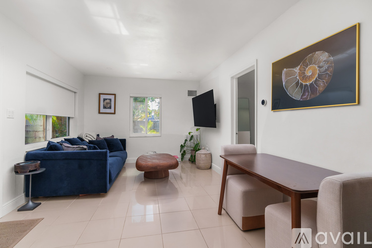 A living room with a blue couch, a wooden table, and a painting of a seashell on the wall.