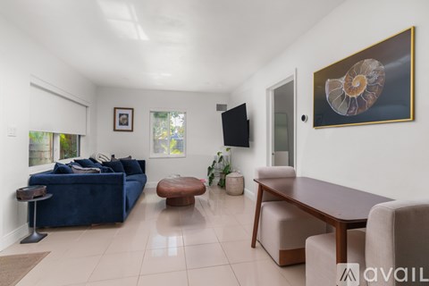 A living room with a blue couch, a wooden table, and a painting of a seashell on the wall.
