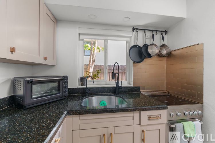 A kitchen with a black microwave, black granite countertop, and a window.