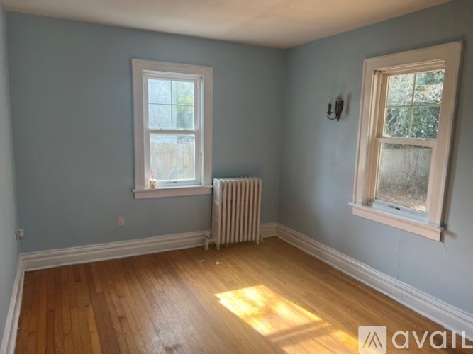 A room with light blue walls, a white window, a white radiator, and a wooden floor.