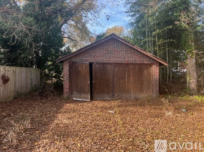 A small brown building with a closed door is surrounded by a fence and trees.