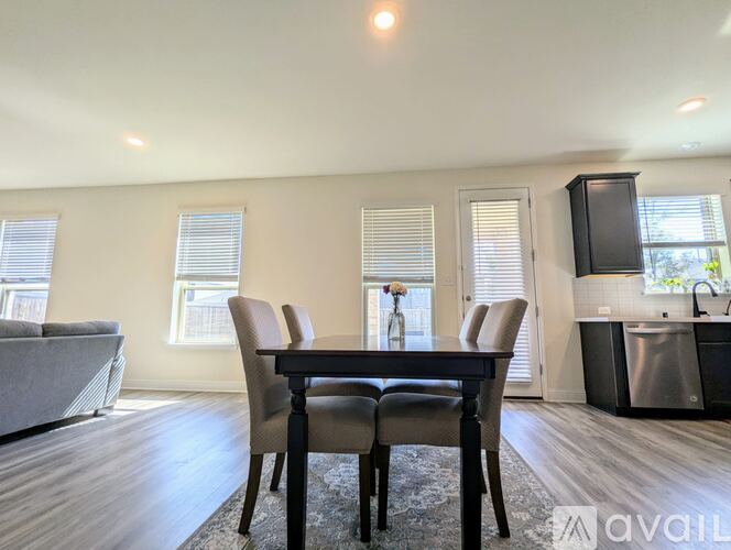 A dining room with a table and chairs in the foreground and a kitchen area in the background.