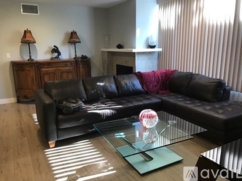 A black leather couch with a glass coffee table in front of it.
