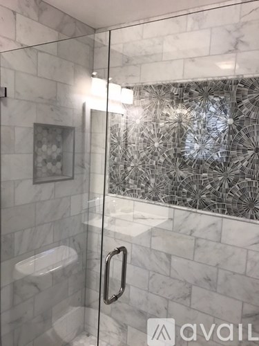 A bathroom with a glass shower door and a marble wall.