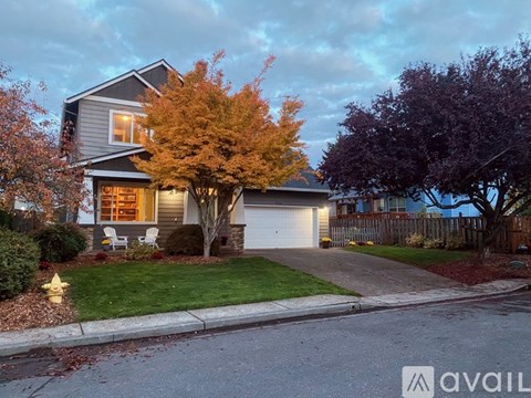 A house with a grey roof and a white garage door is surrounded by trees and bushes.